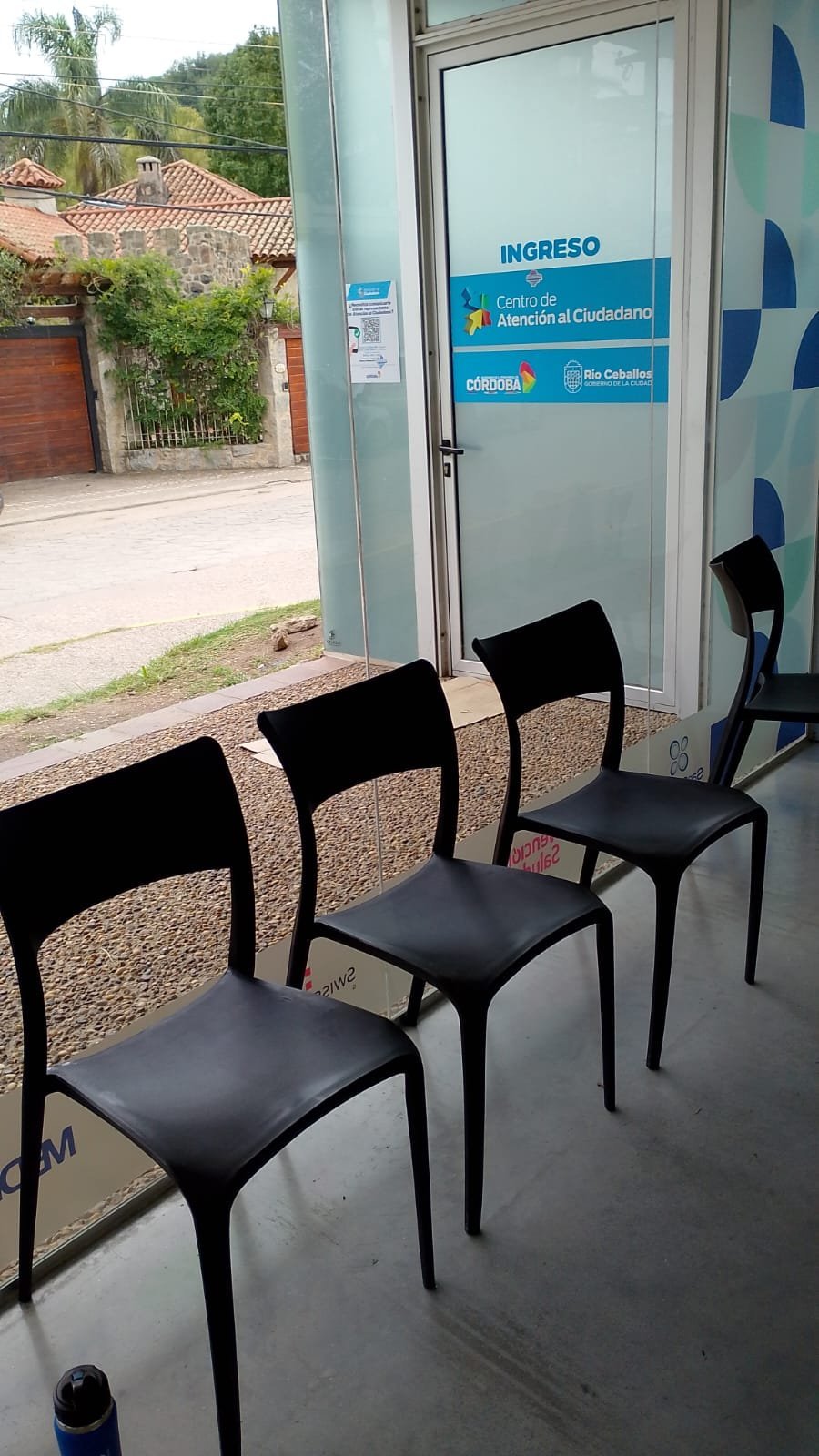 Three black chairs in a waiting area with an entrance door labeled INGRESO at a citizen service center in Cordoba