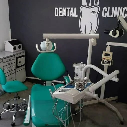 Dental clinic interior with green patient chair, overhead light, white equipment tray, and dark wall with dental clinic signage